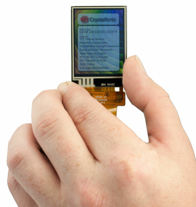 Display shown with a hand for scale. The display is roughly the length of the thumb. Text is displayed on the screen but is mostly unreadable.