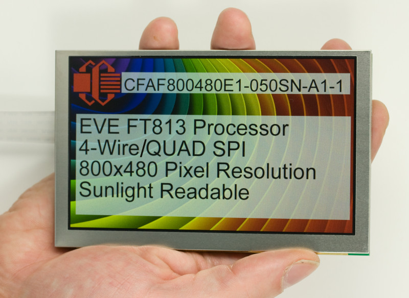 A 5 inch LCD TFT held in a hand for scale. Display shows a rainbow screen, the Crystalfontz logo, and text:
CFAF800480E1-050SN-A1-1
EVE FT813 Processor
4-Wire/QUAD SPI
800x480 pixel resolution
Sunlight Readable