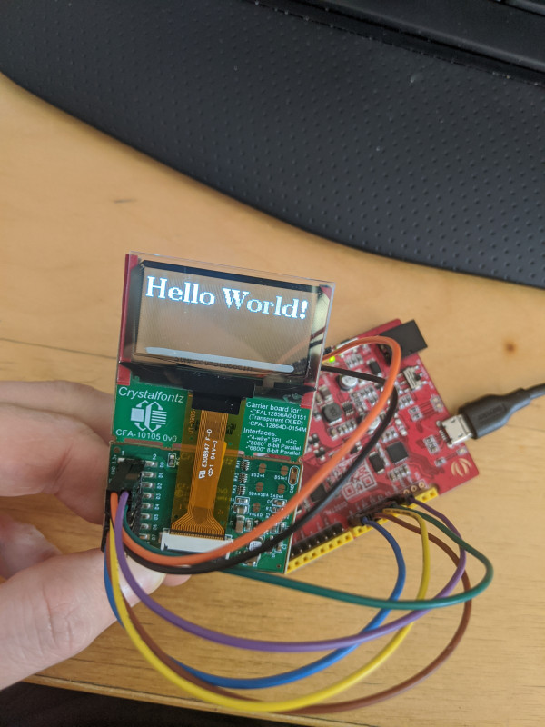 The transparent OLED on the CFA10105 oled breakout board connected to a seeeduino. The OLED is displaying the words "Hello World!"