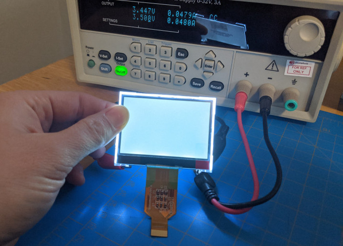 hand holding lit display. Behind display is power supply set to 3.5 v and 0.048mA. Leads from power supply can be seen connected behind display