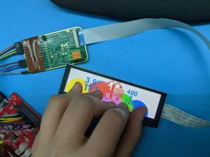 Display connected to a PCB. A hand is touching the display with five fingers. At each touch point, the display is showing a different colored circle. The display also says "3.9"" and shows the Crystalfontz logo