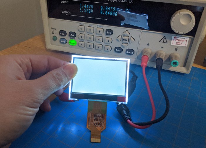 hand holding lit display. Behind display is power supply set to 3.5 v and 0.048mA. Leads from power supply can be seen connected behind display