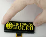 128x32 pixel monochrome yellow graphic OLED. Front View, in hand to show size and perspective.