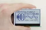 128x64 Backlit Monochrome LCD display, in hand to show size and perspective.