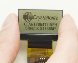 128x64 Transflective monochrome LCD module, front view in hand to show perspective. powered on.